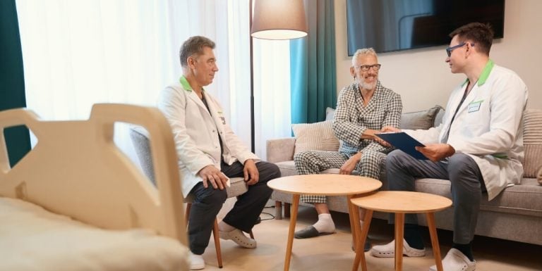 Two Male Nurses Sitting with an Elderly Man in Pajamas for a Health Discussion at an Assisted Living Facility