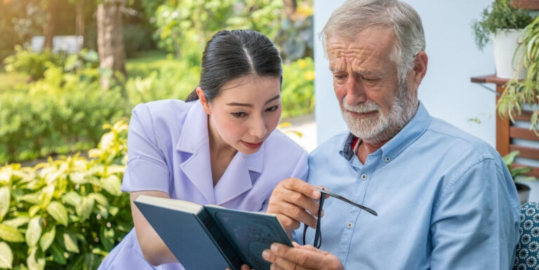 Skilled Nurse Reading Book With Resident at Memory Care Facility