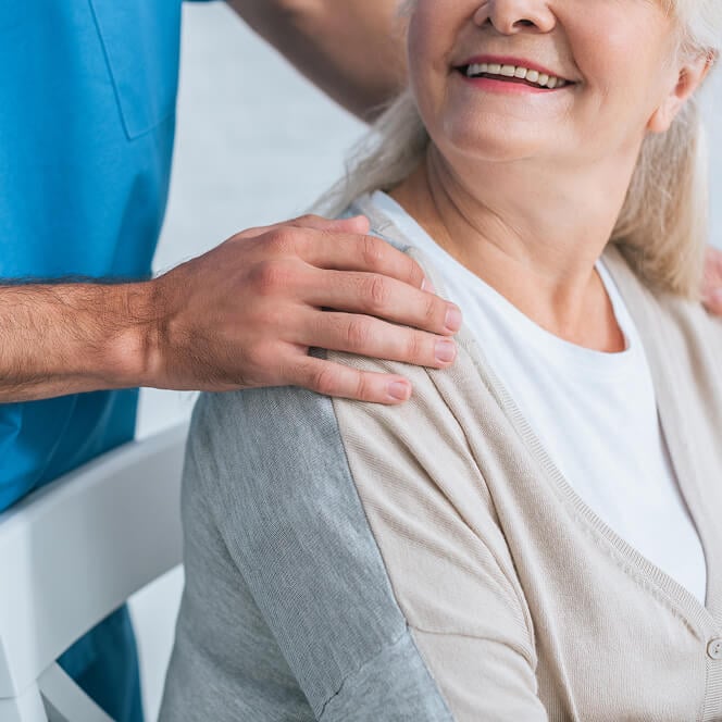 Male Nurse Gently Rests Hand on Smiling Elderly Woman’s Shoulder Male Nurse Gently Rests Hand on Smiling Elderly Woman’s Shoulder